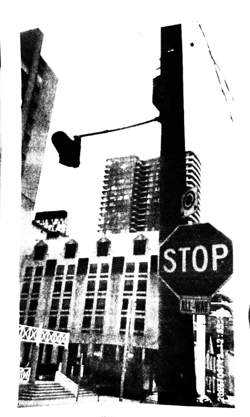An all-way stop sign and a traffic light before an apartment tower.