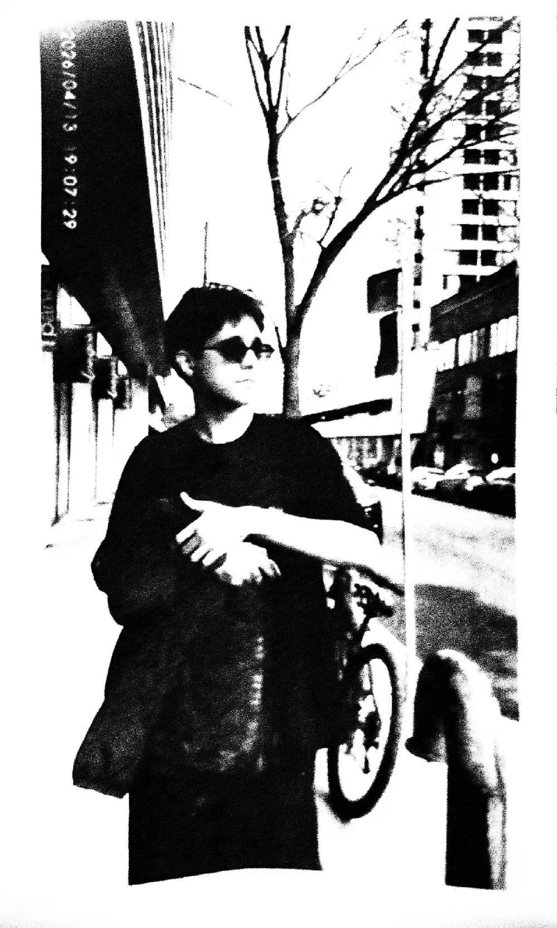 A man in sunglasses walking a bicycle along a sidewalk, 13 April 2026.