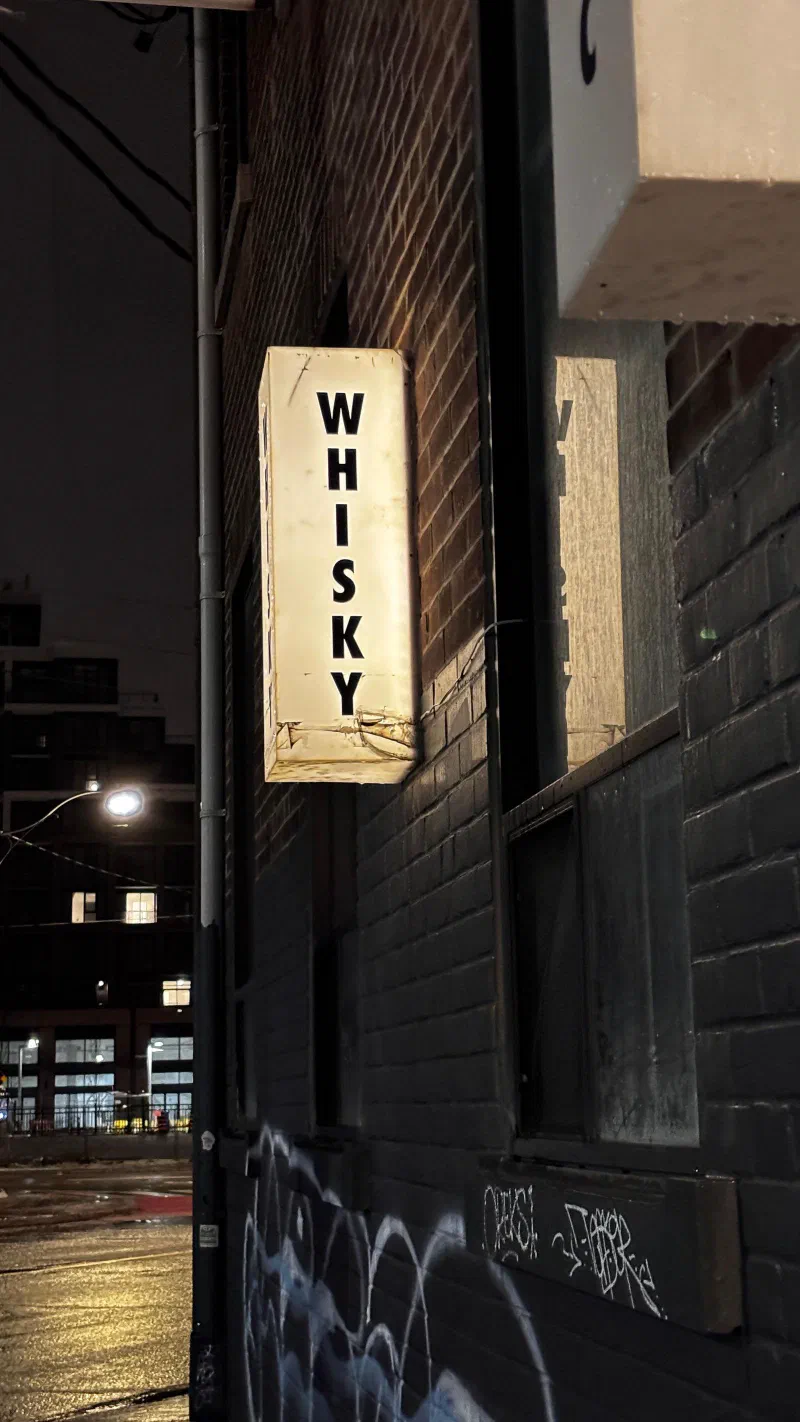 A lit WHISKY sign on a brick wall at night, March 2026.
