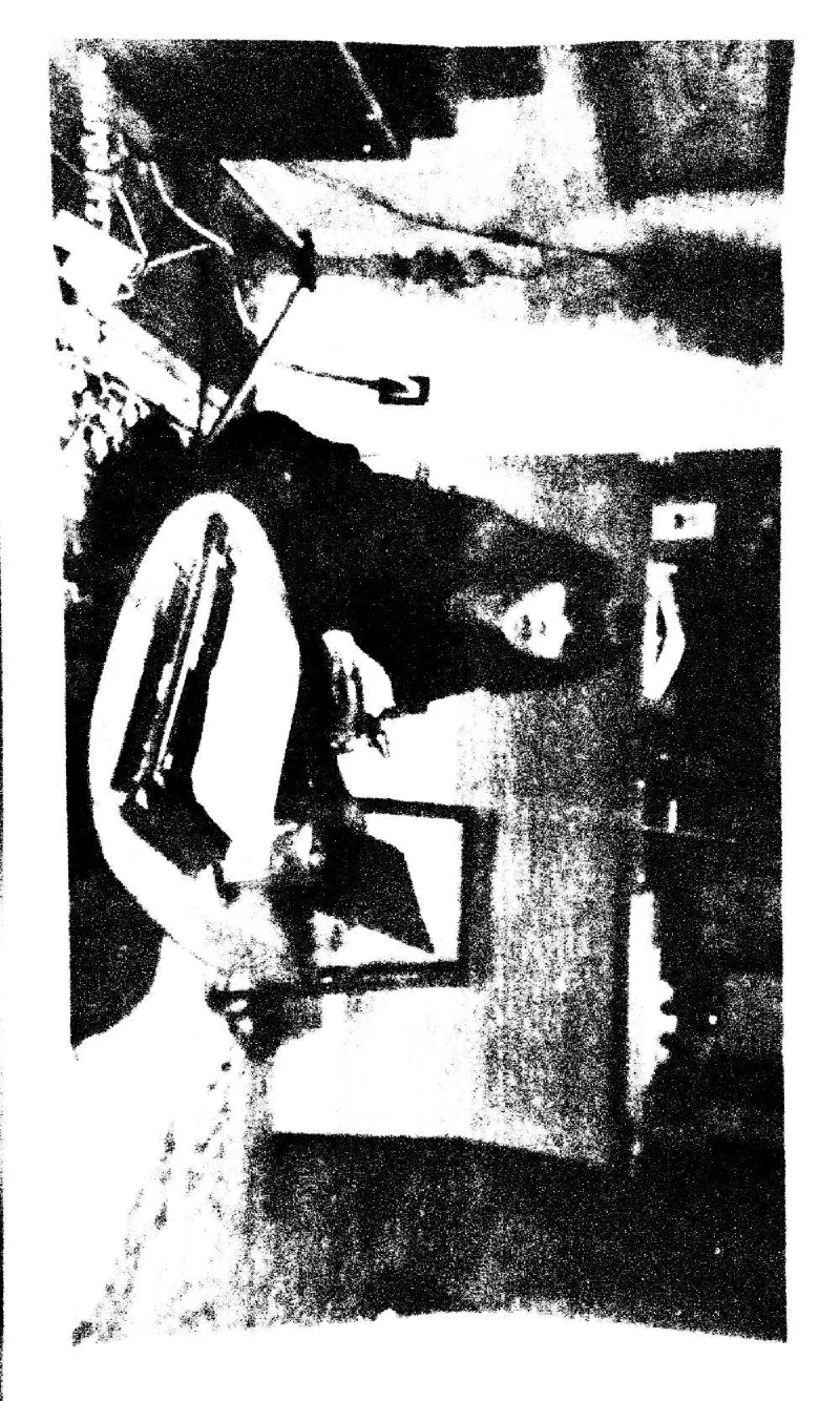 A seated figure in a cluttered interior, in high-contrast black and white.