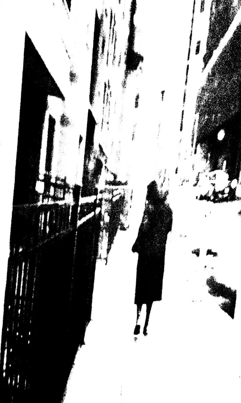 A woman walking down a narrow street lined with railings.