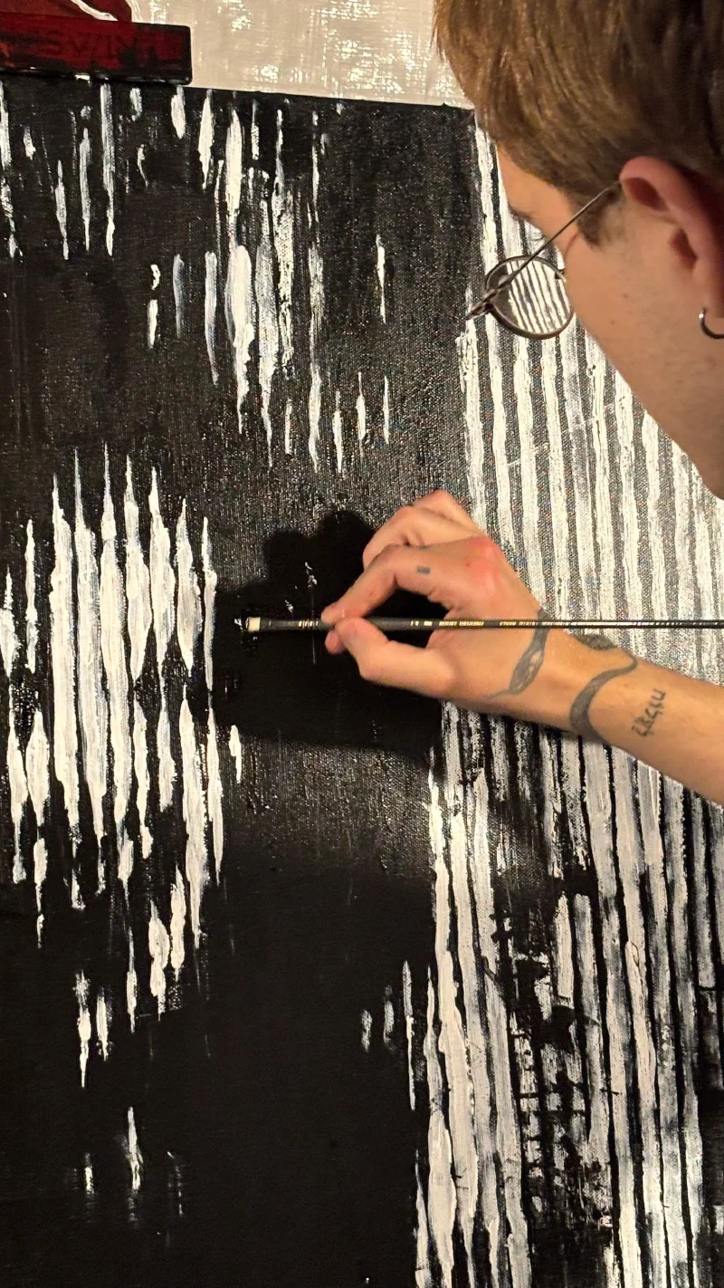 Andrada painting fine white lines into a black canvas, February 2026.