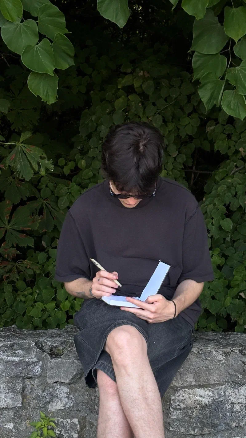 Andrada sketching in a pocket notebook on a stone wall, August 2026.