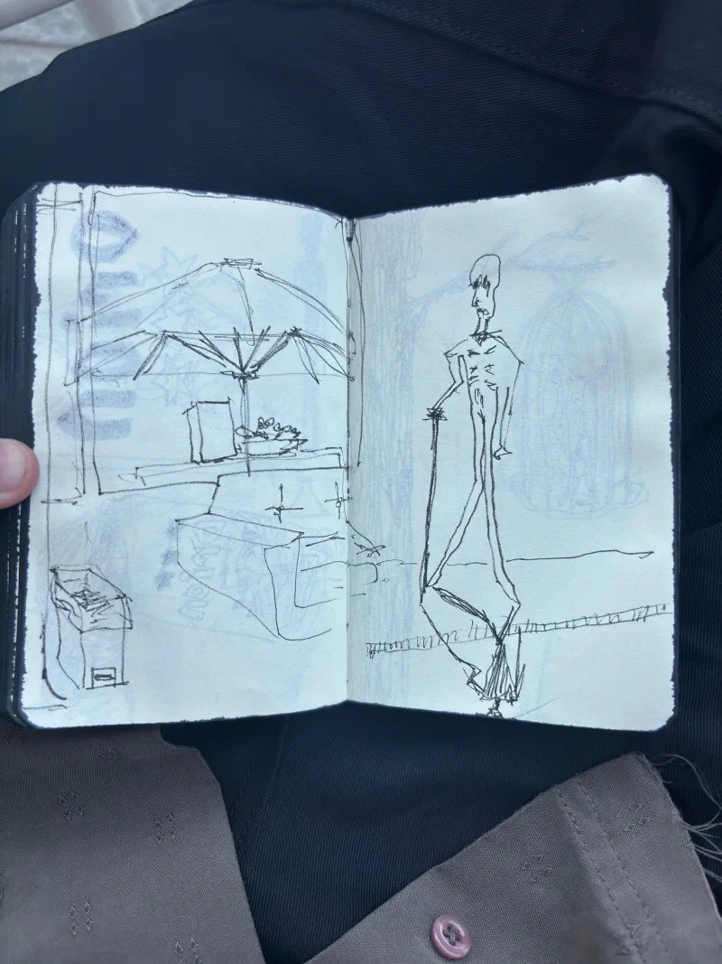 A sketchbook spread: a café table under an umbrella, and a tall, thin figure, July 2026.